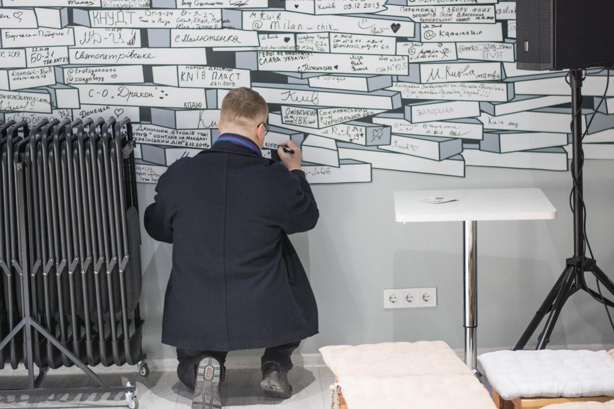 Підпис на згадку. Стіна відтворює складений на Майдані мур із дерев'яних цеглинок, на яких написано назви рідних місць протестувальників